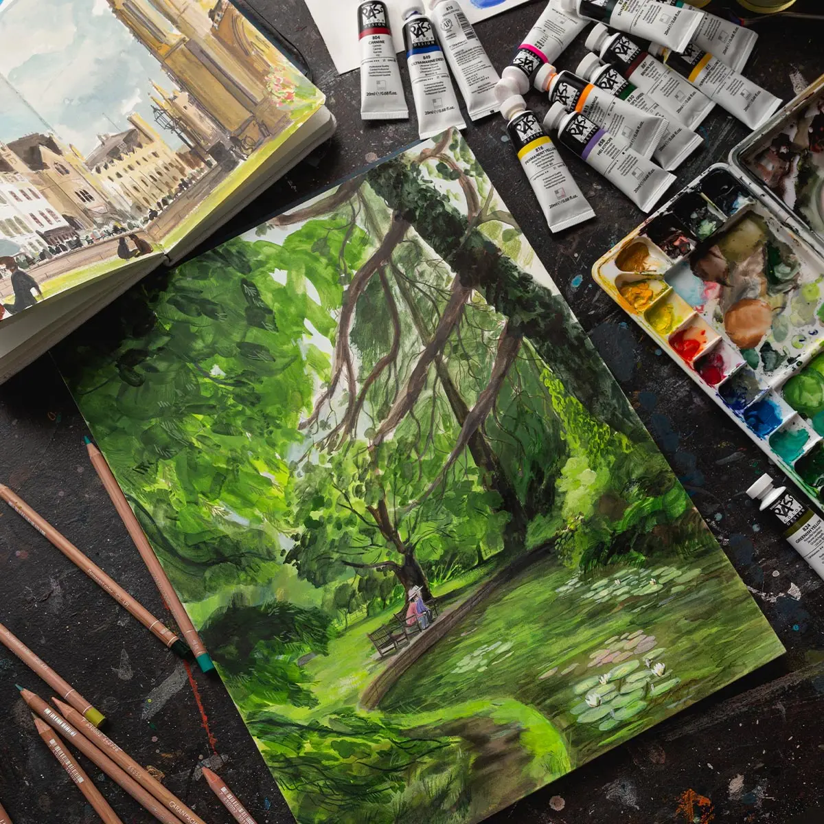 A artist studio, with a painting, gouache in a palette, coloured pencils