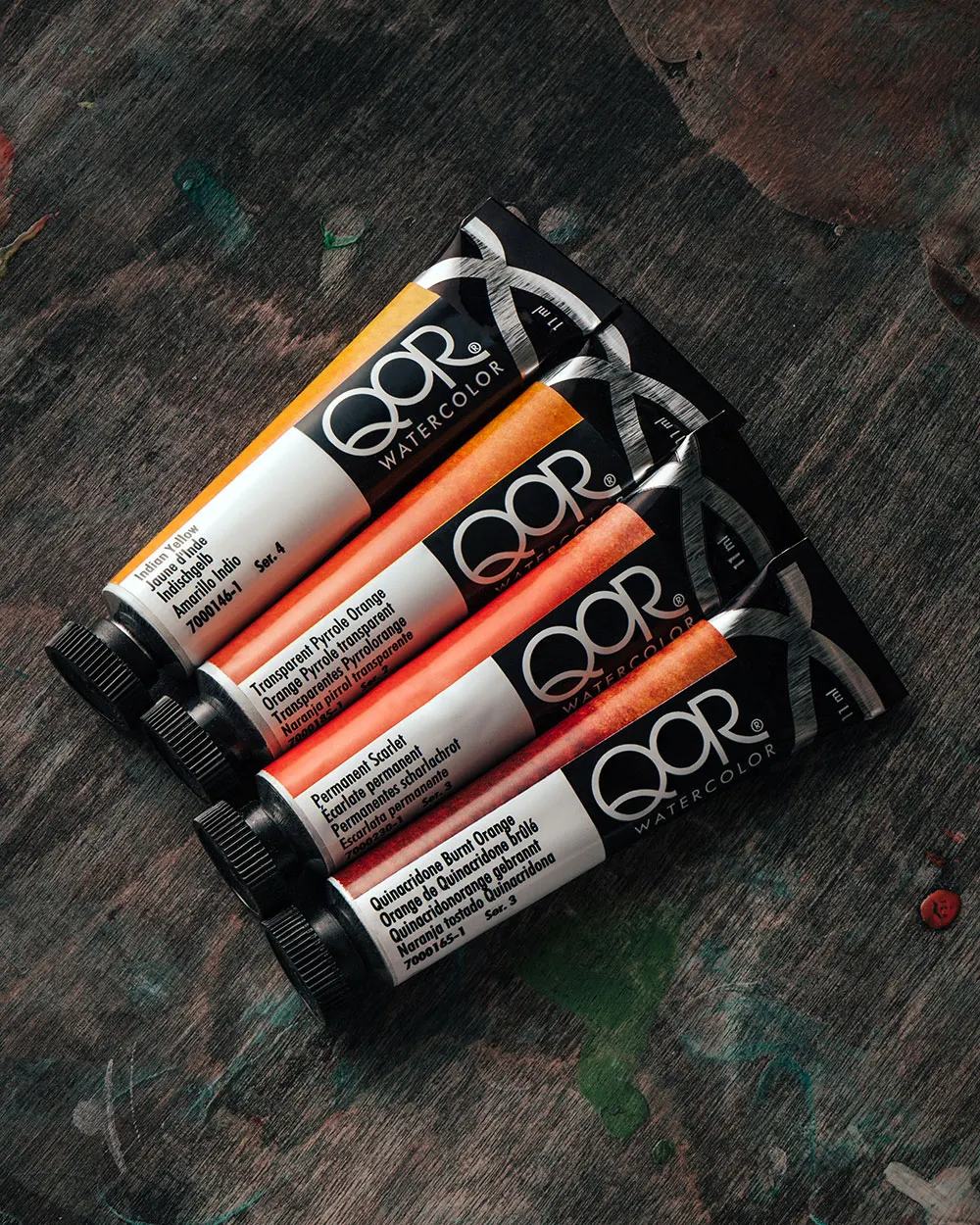 Pink and yellow QOR paint tubes on a dark studio table