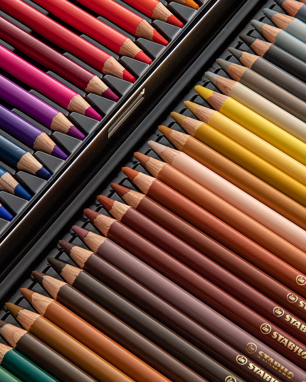 Close-up of neatly arranged Stabilo coloured pencils in a variety of vibrant shades, organized in a black case with a mix of warm, cool, and neutral tones.