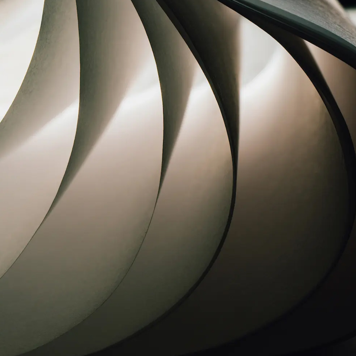 A close-up image of curved sheets of paper layered together, creating a wave-like pattern with soft shadows and highlights. The light interacts with the paper's smooth surface, giving the composition an abstract and serene feel.